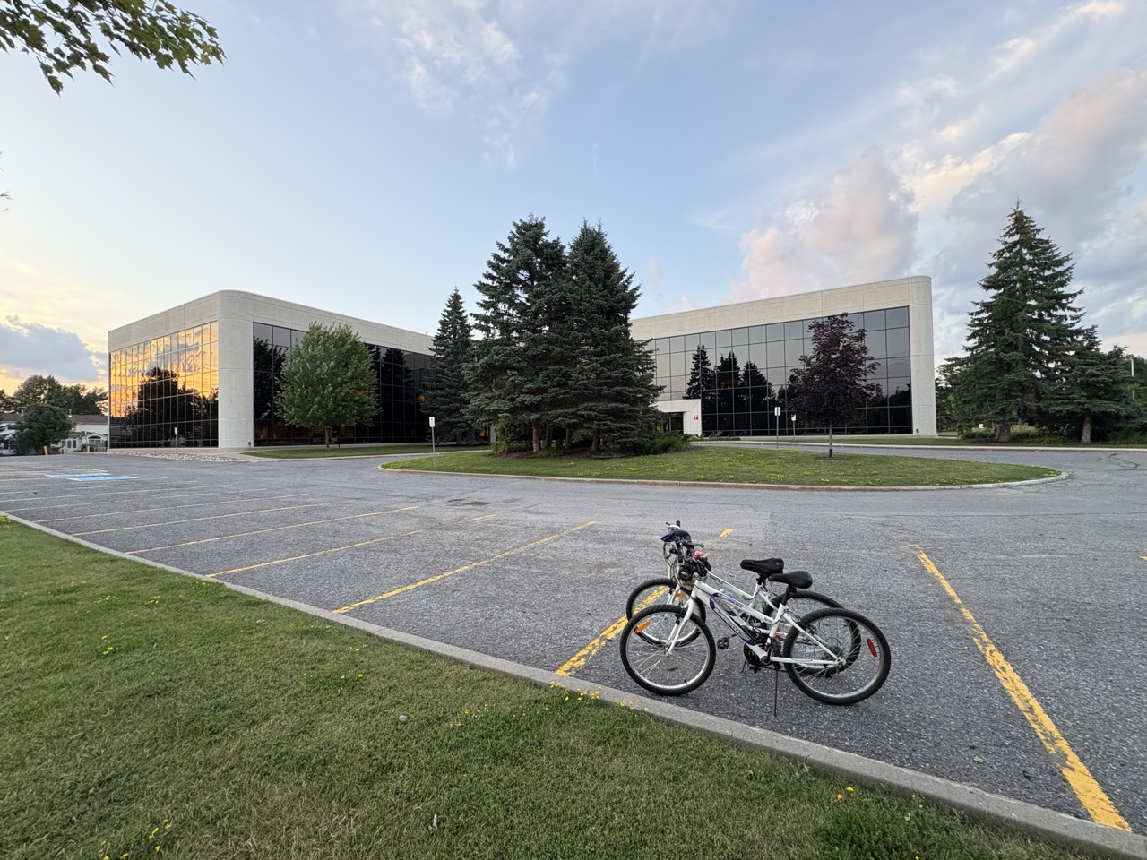 Two bikes in front of a corporate building parking lot